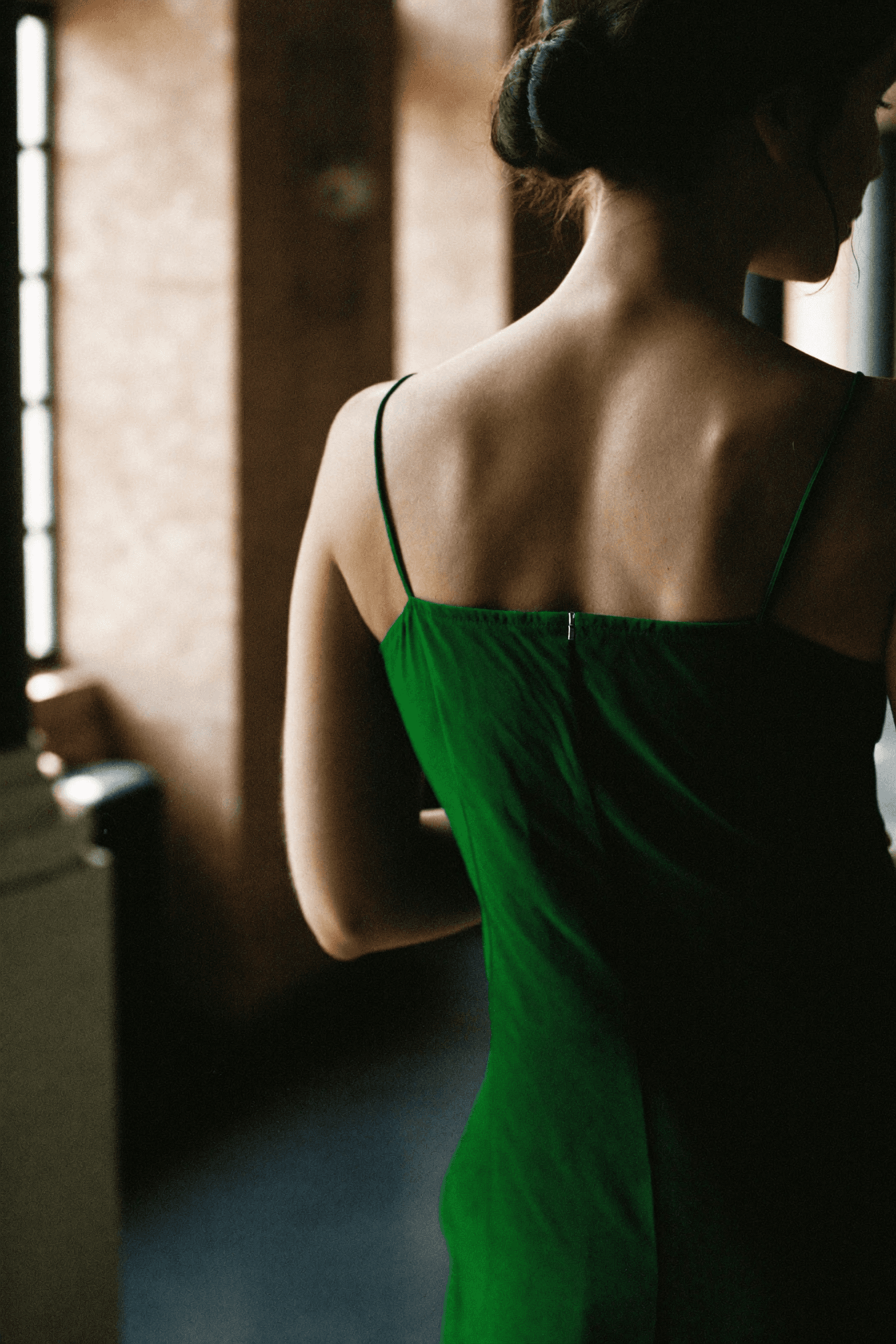 Schiena anonima di donna in vestito verde di seta, capelli raccolti, palazzo romano sullo sfondo.