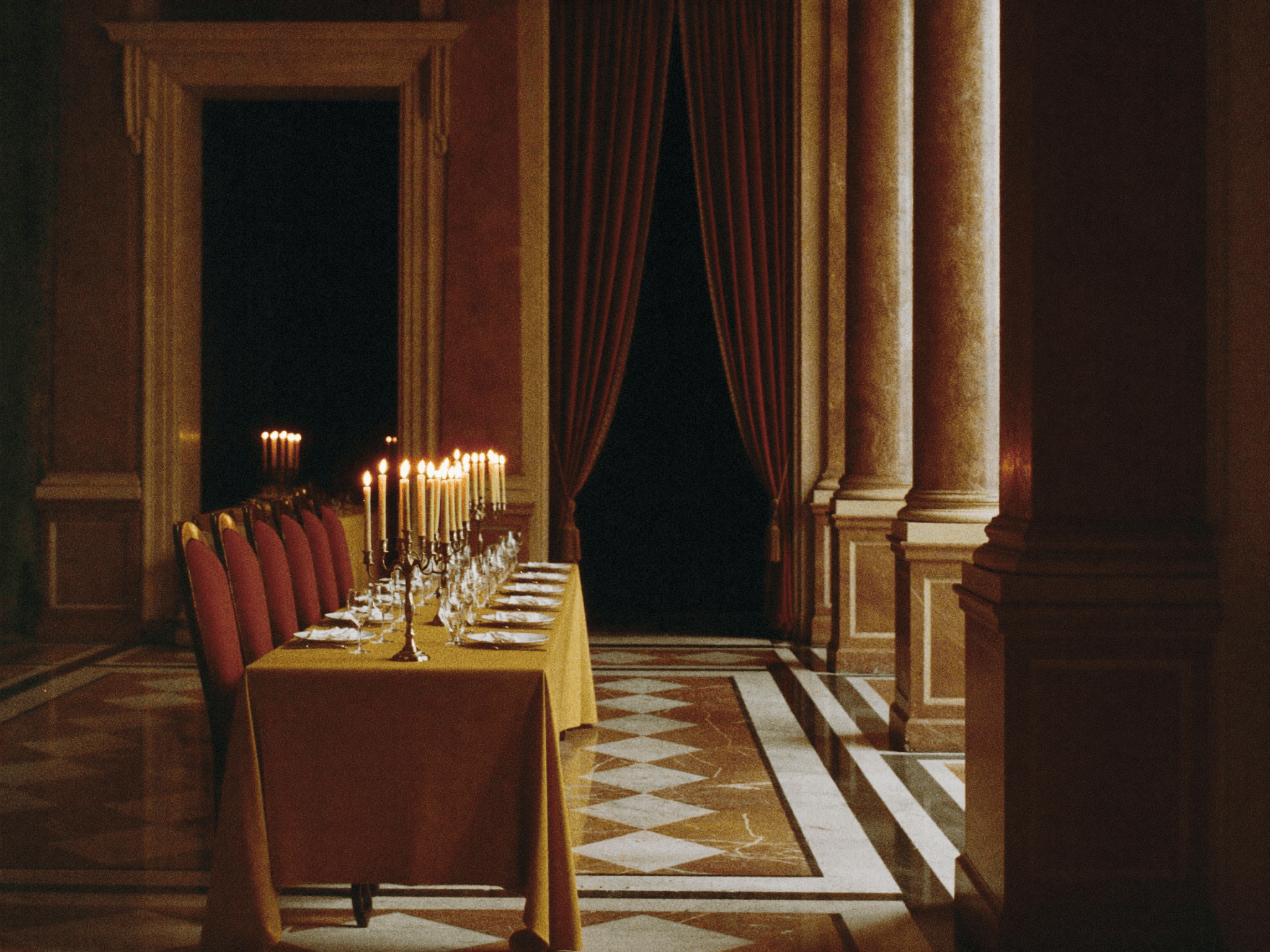 Sala da banchetto di un palazzo italiano, una lunga tavola apparecchiata illuminata da molte candele, nessuno presente.