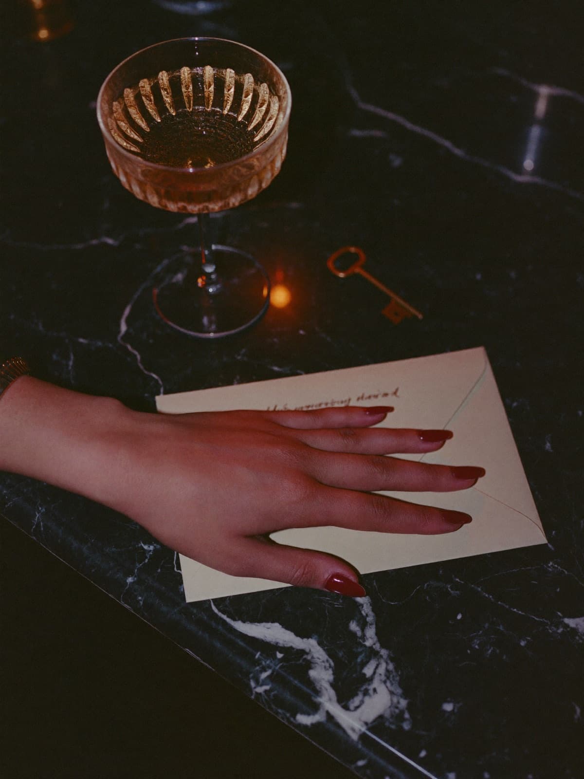 Mano femminile su una busta color crema accanto a una coupe di spumante