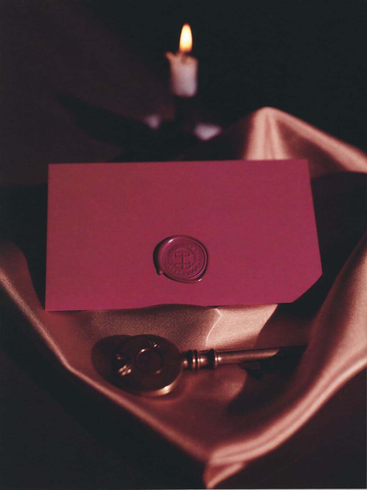 Invito sigillato con ceralacca magenta su seta champagne, accanto a una chiave d'ottone